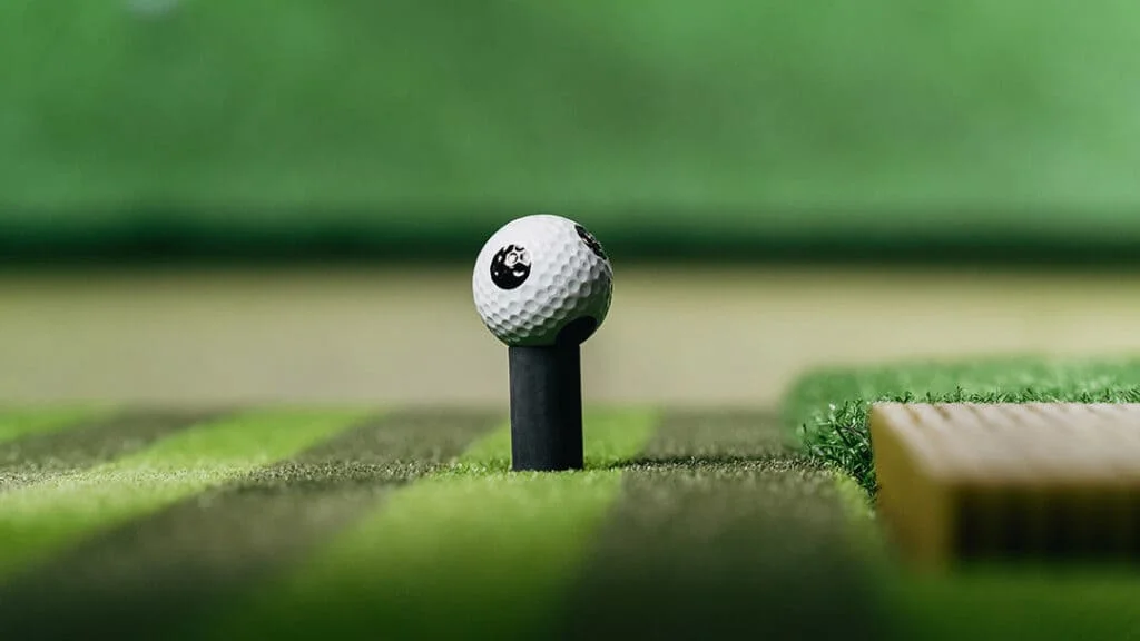 A golf ball raised on the automatic tee, turf in soft focus